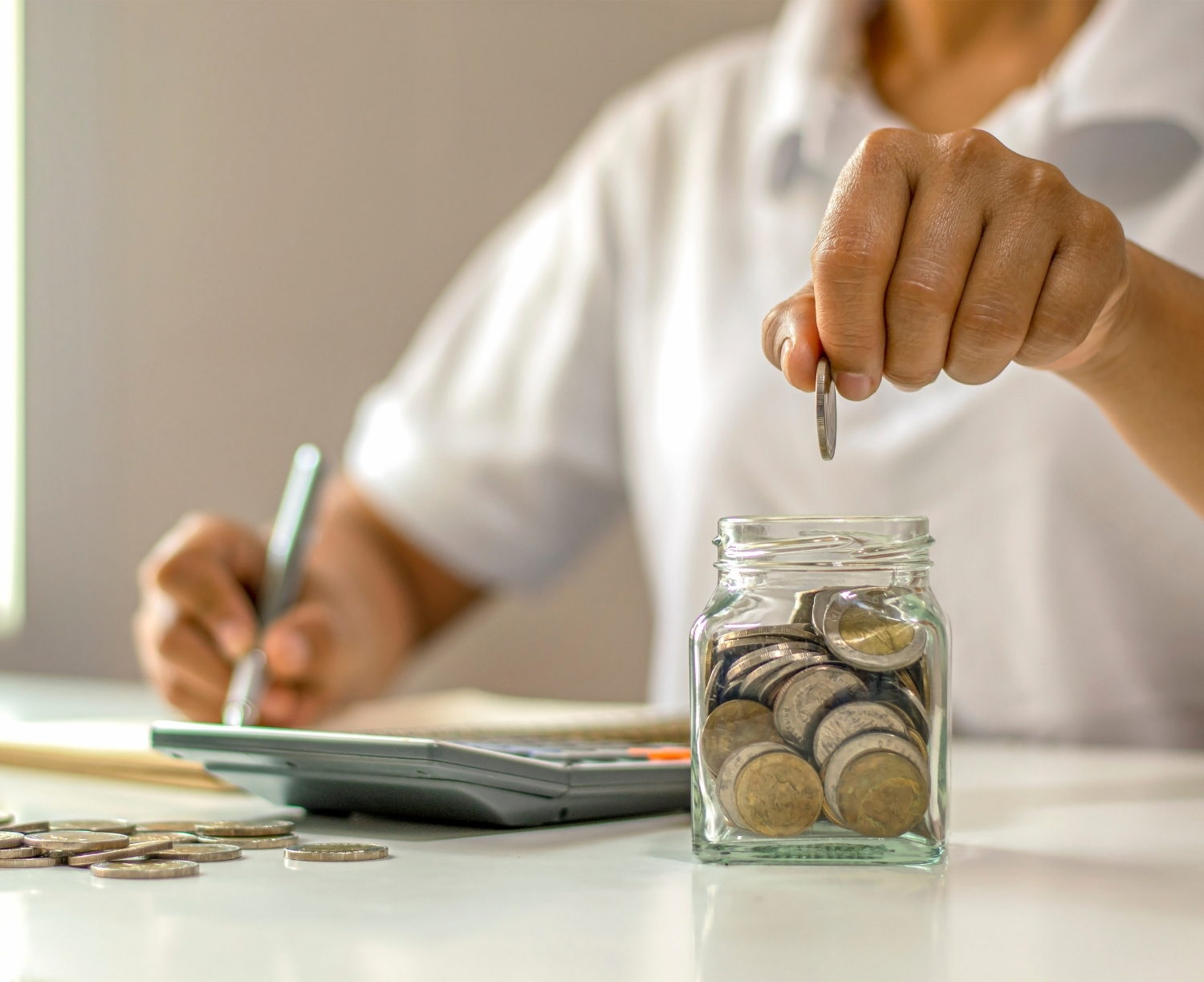 Person adding coins to a savings jar beside a calculator while budgeting for moving costs.